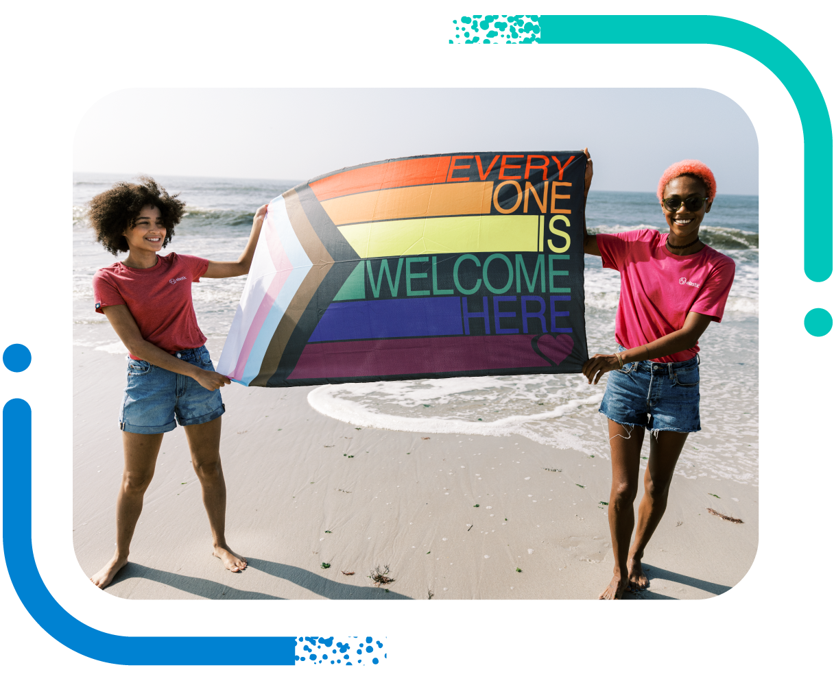 Two women celebrate diversity holding LGBTQ+ Pride flag on a beach