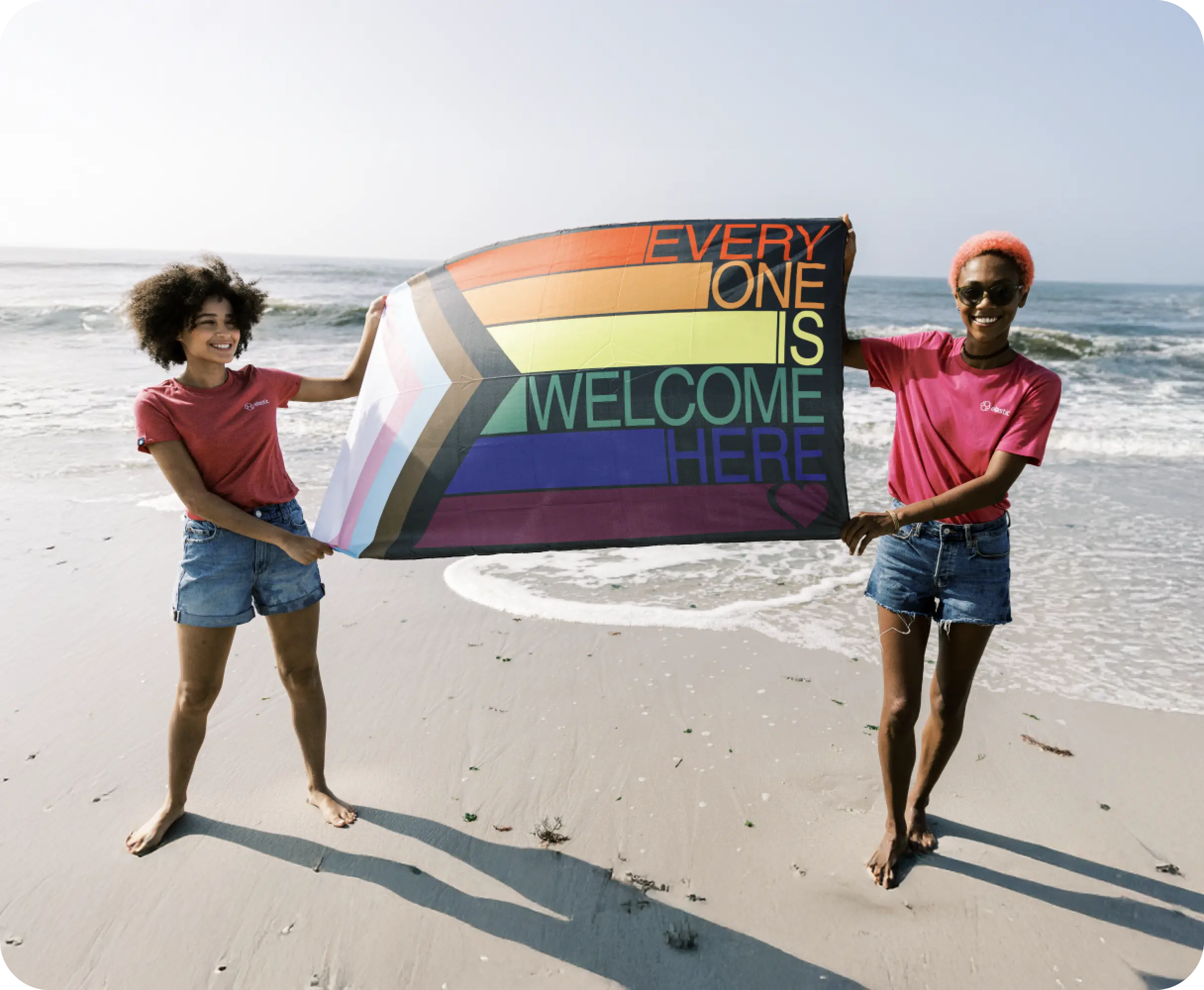 Two women celebrate diversity holding LGBTQ+ Pride flag on a beach